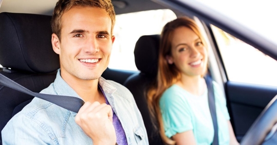 two young people putting on their seatbelts and smiling at the camera
