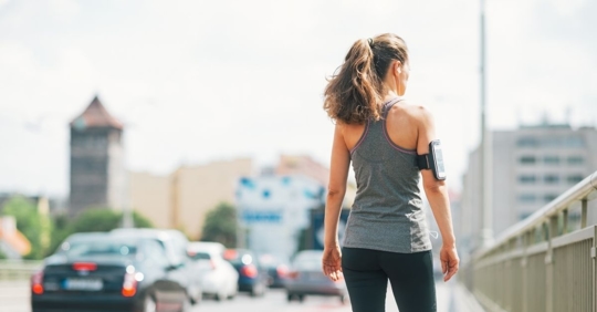 woman in athletic gear walking across a bridge next to a line of cars